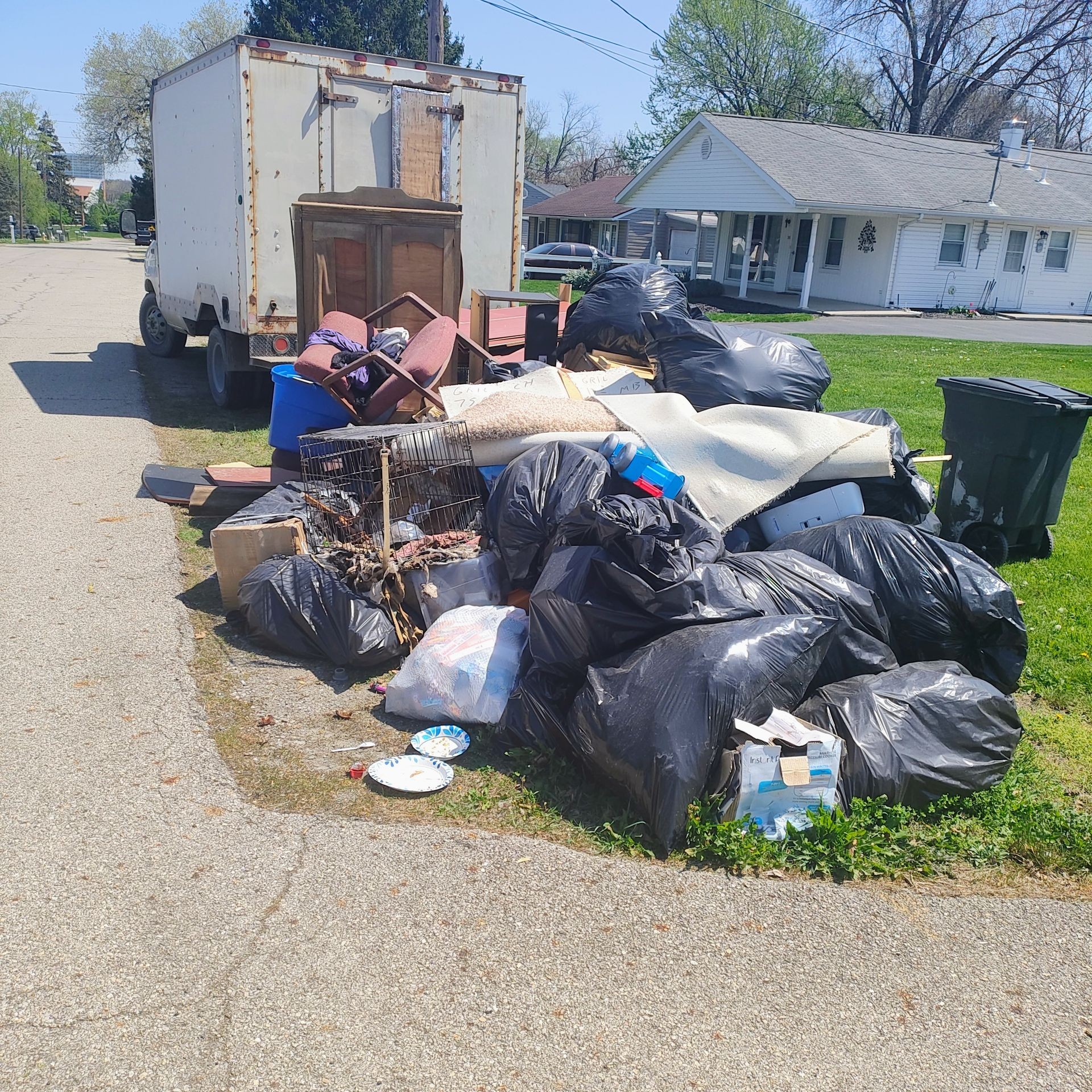 Big pile of trash behind a box truck with a trashcan beside it